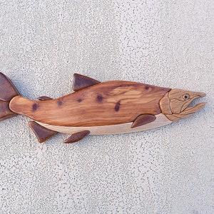 May include: A wooden salmon sculpture with a natural wood finish. The sculpture is carved in detail and has a realistic appearance.