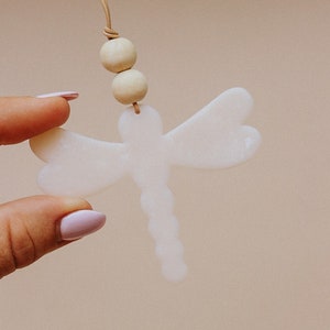 May include: A white ceramic dragonfly pendant with a brown leather cord and two wooden beads.