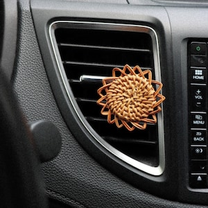 May include: A woven wicker car air freshener in the shape of a flower, hanging from the air vent of a car.