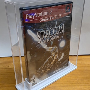Könnte beinhalten: Eine transparente Acryl-Vitrine mit einer PlayStation 2-Videospielhülle. Das Spiel heißt "Star Ocean: Till the End of Time" und zeigt eine Charakterillustration. Die Hülle ist mit "Greatest Hits" beschriftet. Die Vitrine hat einen weißen Sockel.