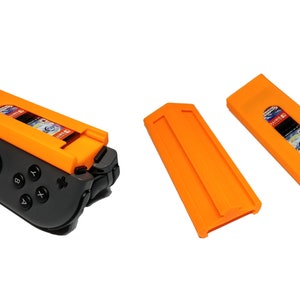 Pode incluir: Suporte para cartão de jogo de plástico laranja para um console Nintendo Switch. O suporte é anexado ao controlador esquerdo Joy-Con e possui uma ranura para um cartão de jogo. Dois suportes laranja adicionais são mostrados separadamente.