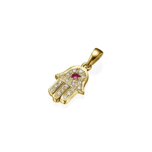 May include: A gold-colored Hamsa hand pendant with a red gemstone center and small white gemstones. The pendant has a loop for a chain and is marked with "750".
