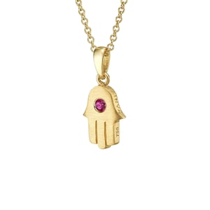 May include: Gold necklace with a Hamsa hand pendant, featuring a central pink gemstone. The pendant has a brushed finish and hangs from a fine chain. The pendant is marked with the number 750.