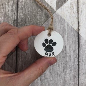 May include: White ceramic pet tag with a black paw print and the name "MAX" written below.
