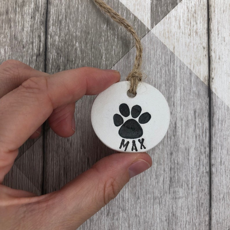 May include: White ceramic pet tag with a black paw print and the name "MAX" written below.