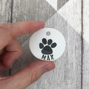 May include: White ceramic dog tag with a black paw print and the name "Max" engraved on it.