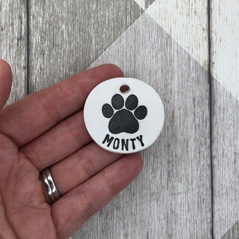 May include: White ceramic dog tag with a black paw print and the name "MONTY" engraved on it.