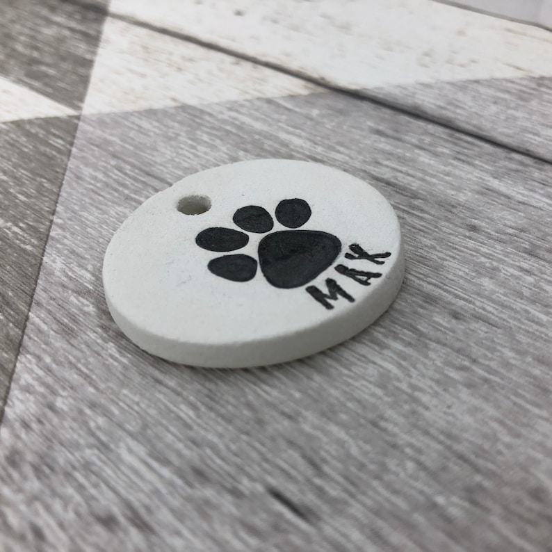 May include: White ceramic dog tag with a black paw print and the name "Max" inscribed on it.