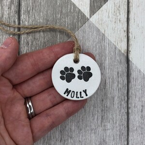 May include: White ceramic ornament with two black paw prints and the name "MOLLY" written below.