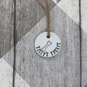 May include: A white ceramic dog treat jar with a bone design and the text "Tilly's Treats".