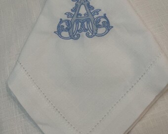 May include: A white linen napkin with a blue embroidered monogram of the letter "A" in a decorative script font.