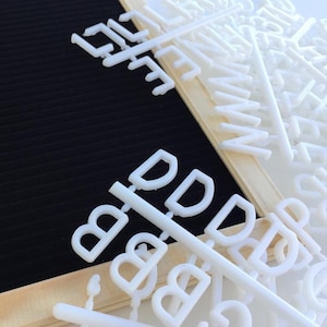 May include: White plastic letters and numbers on a wooden frame. The letters are arranged in a random order and are ready to be used for a message board.