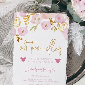 May include: A pink and gold floral themed invitation for a 2nd birthday party. The invitation says "Oh Two-dles" and "It's hard to believe, but yes it's true our Emmalyn is turning 2!" with a pink Mickey Mouse head on each side. The invitation includes the date, time, and location of the party, as well as the RSVP information.