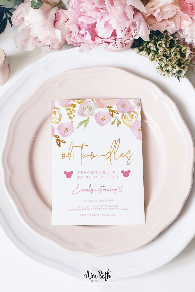 May include: A pink and gold floral themed invitation card with the text "Oh Two-dles" in gold lettering. The text "It's hard to believe, but yes it's true our Emmalyn is turning 2!" is written in pink lettering. The invitation includes details for a birthday party, including the date, time, location, and RSVP information.