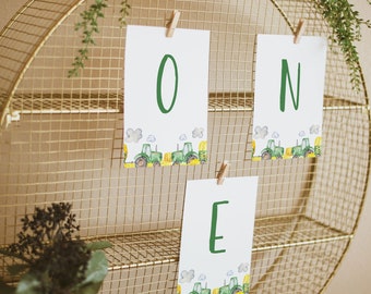 Puede incluir: Una estantería de alambre dorado con tres niveles tiene tres tarjetas blancas con letras verdes que deletrean "ONE". Cada tarjeta tiene un borde de tractores verdes y campos amarillos.