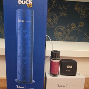 May include: A tall blue Disney Donald Duck 90th anniversary box containing a cylindrical scent diffuser, alongside a smaller white box labeled Smart Car Diffuser, a small bottle of fragrance oil, and a black Star Wars branded box.