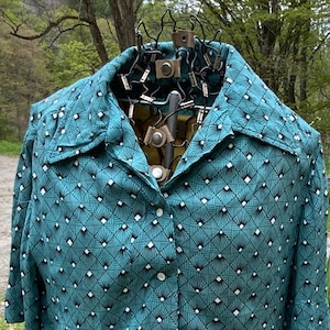 May include: A teal blue short-sleeved button-up shirt with a geometric pattern of black and white diamonds. The shirt has a collar and a button-up front.