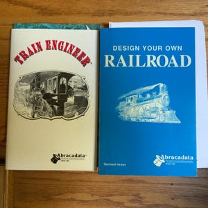 Peut inclure: Deux manuels de logiciels avec des couvertures blanches et bleues. Le manuel de gauche est intitul&eacute; Train Engineer avec une illustration en noir et blanc d'un train. Celui de droite est intitul&eacute; Design Your Own Railroad avec un train bleu et blanc.