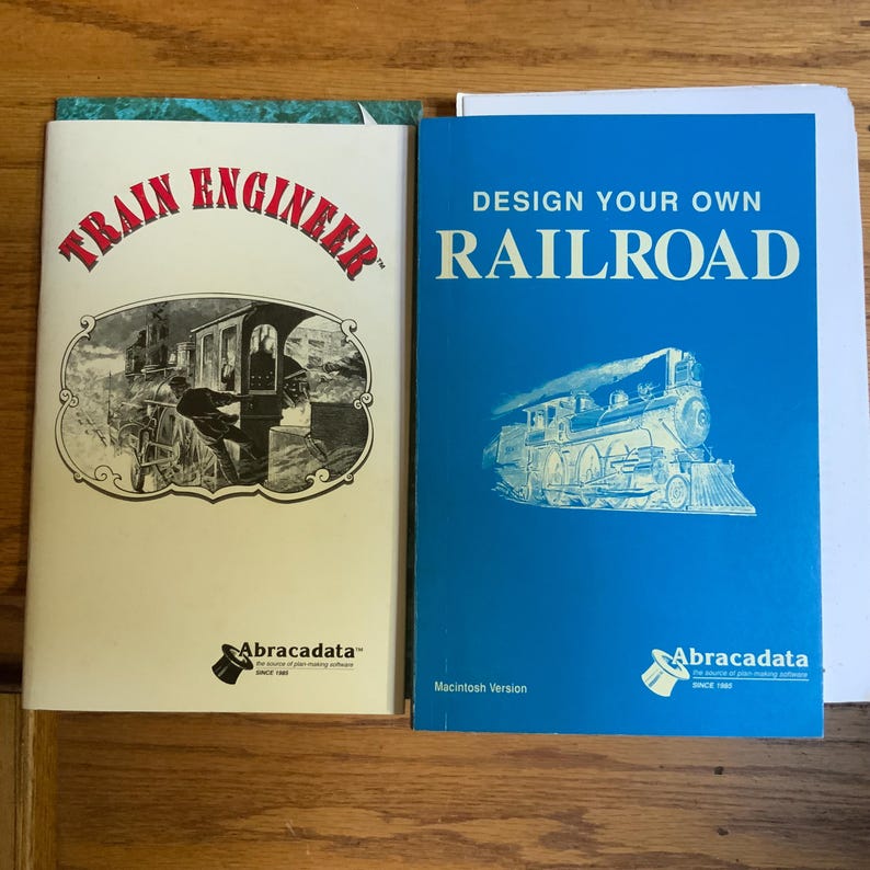 Peut inclure: Deux manuels de logiciels avec des couvertures blanches et bleues. Le manuel de gauche est intitul&eacute; Train Engineer avec une illustration en noir et blanc d'un train. Celui de droite est intitul&eacute; Design Your Own Railroad avec un train bleu et blanc.