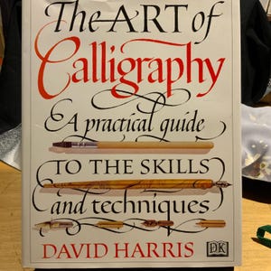 May include: A book titled "The Art of Calligraphy" with red and black lettering. The cover features a calligraphy pen and brush illustration. The book is a practical guide to skills and techniques by David Harris.