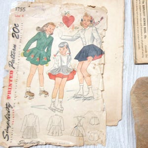 May include: Vintage Simplicity sewing patterns, featuring illustrations of girls in ice skating outfits. The patterns are printed on aged paper, with the price of 20 cents visible. A Simplicity Primer booklet is also present.