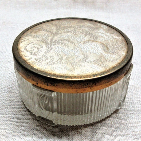 Lidded  glass trinket dish is 3.5" diameter and 2" tall. Metal lid has a satin woven fabric under a plastic cover. Good used condition.