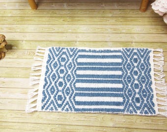 May include: A blue and white woven rug with fringe on the edges. The rug has a geometric pattern and is perfect for adding a touch of style to any room.