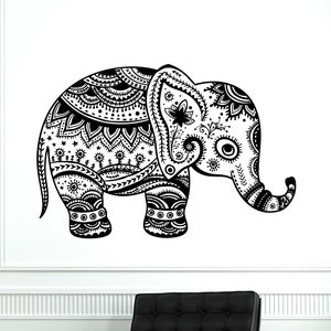 Puede incluir: Un vinilo decorativo de pared con un elefante en blanco y negro con intrincados patrones simétricos. El elefante está de pie, con la trompa enrollada. El vinilo está en una pared blanca, encima de una silla de cuero negro con base cromada.