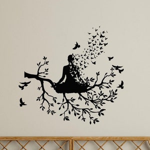 May include: Black and white silhouette wall decal of a woman sitting in a yoga pose on a tree branch with birds flying around her.