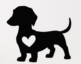 May include: A black dachshund silhouette with a white heart-shaped detail on its chest. The dog is standing, facing left, with its tail curved upwards. The image is a wall decal or sticker, suitable for a nursery or pet-themed room.