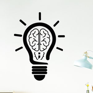 May include: Black and white wall decal of a light bulb with a brain inside. The light bulb has a stylized design with a filament and a base. The brain is detailed with folds and ridges. The decal is on a white wall with a desk and lamp in the background.