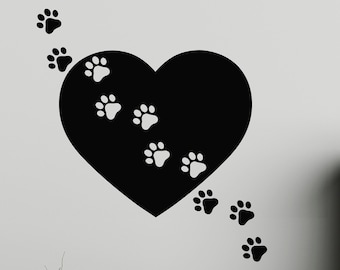 May include: Black and white wall decal of a heart with paw prints coming out of it. The decal is on a white wall with a couch and a table in the background.