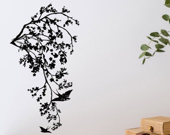 May include: Black silhouette of a tree branch with white blossoms and two birds in flight against a white wall. The wall is decorated with a black and white floral design.