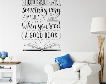 Puede incluir: Una pared blanca con una cita en blanco y negro que dice "Creo que algo muy mágico puede suceder cuando lees un buen libro". La cita está acompañada de una ilustración en blanco y negro de un libro abierto. Un sillón blanco con un cojín azul está en primer plano.