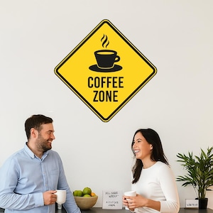 May include: A yellow diamond-shaped sign with a black coffee cup icon and the words "COFFEE ZONE" in black text. Two people are standing in a kitchen, smiling and holding white mugs. A coffee maker and a plant are also visible.