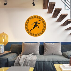 May include: A circular wall sticker depicting a black silhouette of an athlete with a torch on an orange backdrop, framed by a Greek key pattern. The sticker is affixed to a white wall, suitable for home decor.