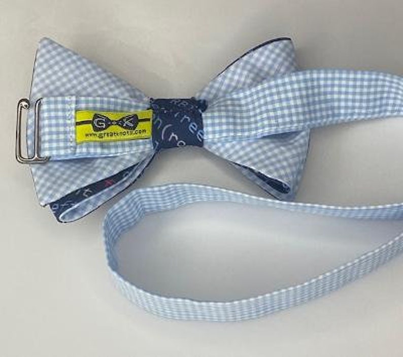 May include: A blue and white gingham bow tie with a blue and white gingham strap. The bow tie has a yellow label with the text "GK" and "www.greatknots.com".