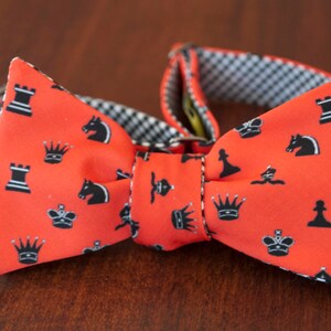 May include: A red bow tie with a black and white chess piece pattern. The bow tie has a black and white checkered pattern on the back.