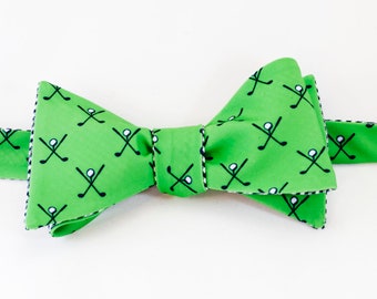 May include: A green bow tie with a white and black golf club pattern. The bow tie has a white and black checkered trim.