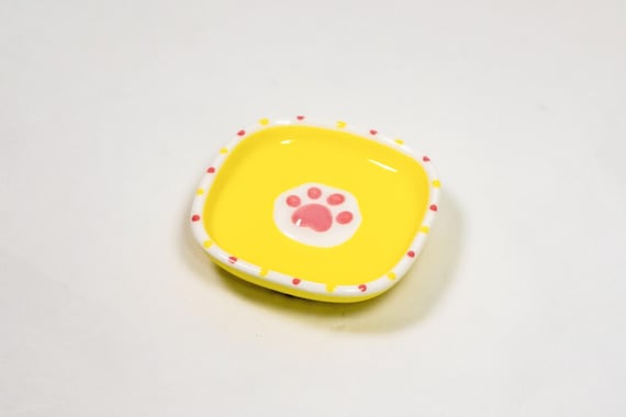 A ceramic dish sculpted as a raised cat paw — surprisingly detailed and actually useful as a sauce cup or ring dish for cat people.