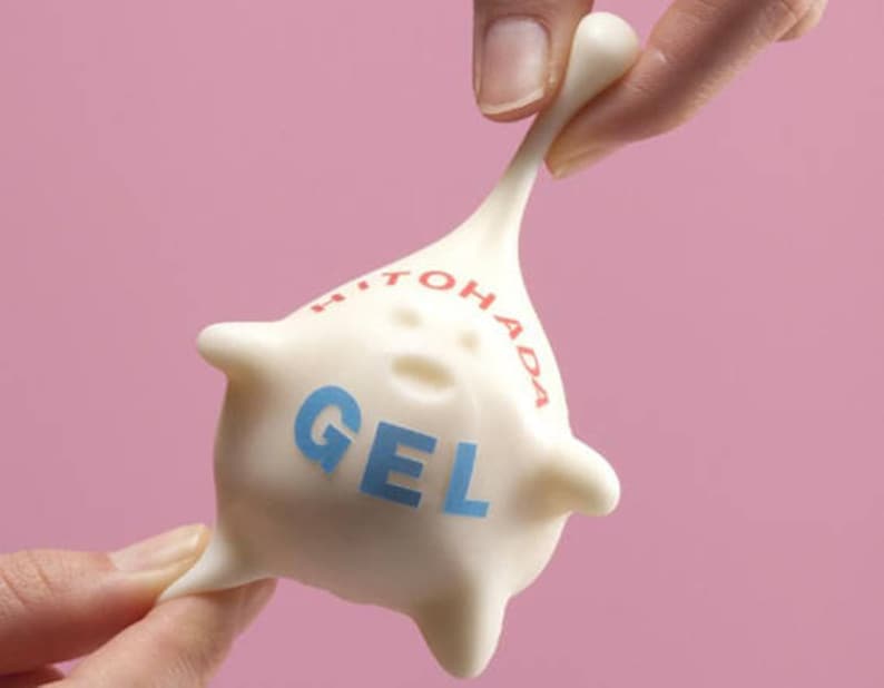 K&ouml;nnte beinhalten: Wei&szlig;es gelartiges Spielzeug mit der Aufschrift "HITO HADA GEL". Das Spielzeug wird von einer Hand gedehnt und gezogen.