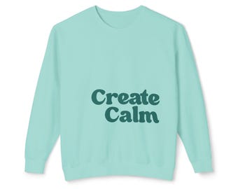May include: A light mint green long-sleeve sweatshirt featuring the text "Create Calm" printed in a dark forest green, rounded, bold font on the front. The garment has a crew neckline, long sleeves with ribbed cuffs, and a ribbed hemline.