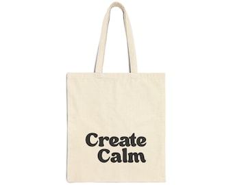 May include: Cream-colored tote bag with the words "Create Calm" printed in black, bold, rounded letters. The bag has two matching handles for carrying and is made of a sturdy fabric.