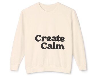 May include: A cream-colored long-sleeve sweatshirt featuring the text "Create Calm" printed in a dark brown, rounded, bold font across the center of the chest. The garment has a crew neckline, ribbed cuffs, and a ribbed hemline.