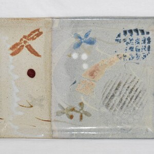 May include: A rectangular ceramic serving tray with a light brown glaze on one side and a light blue glaze on the other side. The tray is decorated with abstract designs in shades of brown, blue, white, and red.