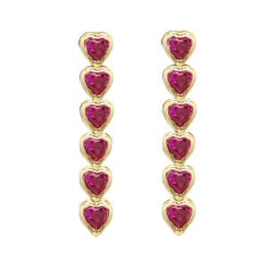 Puede incluir: Un par de pendientes dorados con cinco gemas rojas en forma de corazón. Cada pendiente presenta una serie de corazones colgantes. El fondo es blanco, resaltando la joyería.