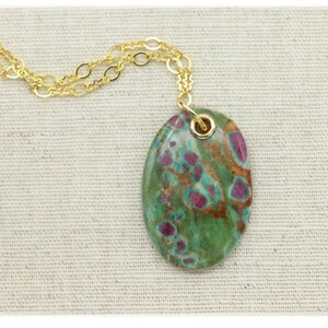 May include: A gold chain necklace with a green and pink oval pendant. The pendant is made of a natural stone with a unique pattern.