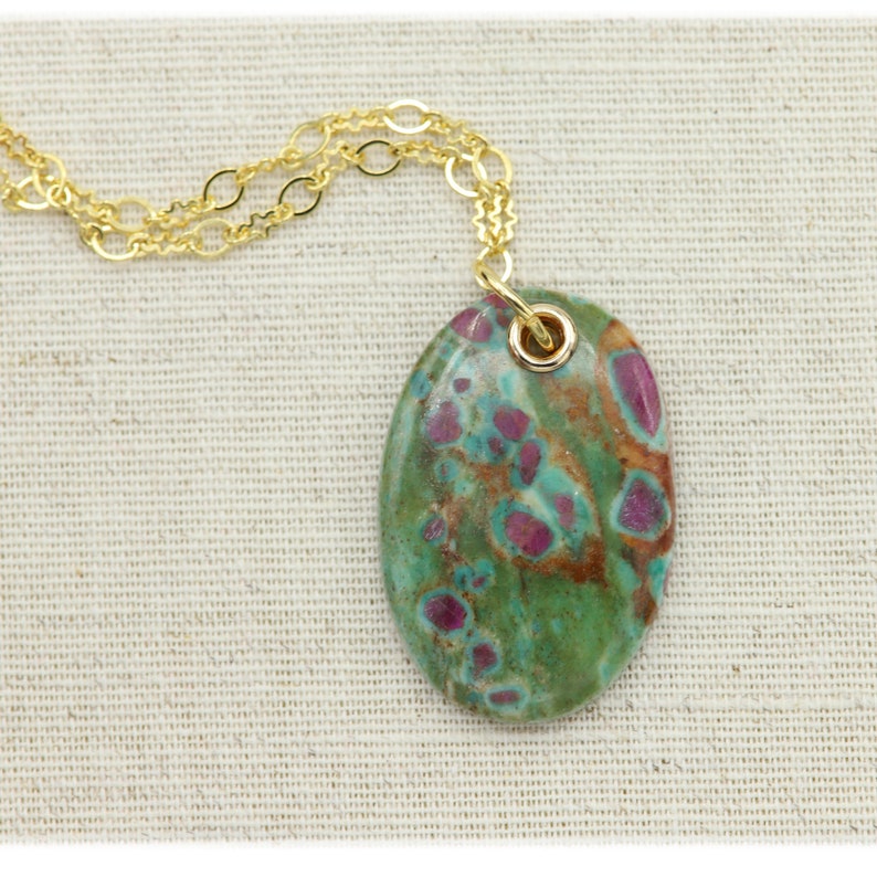 May include: A gold chain necklace with a green and pink oval pendant. The pendant is made of a natural stone with a unique pattern.