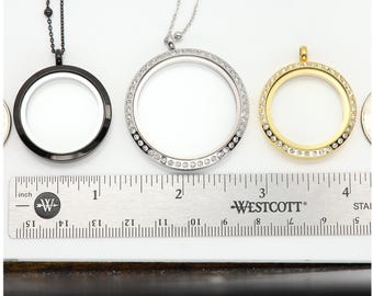 May include: Three silver locket necklaces with a clear glass insert and a row of clear crystals around the edge. The lockets are shown on a white surface with a ruler for size comparison. The ruler is marked in inches.