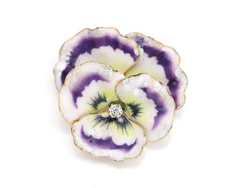 May include: A floral brooch in the shape of a pansy. The brooch features petals in white, purple, and yellow with a gold-colored trim. A small, round diamond is set in the center of the flower.